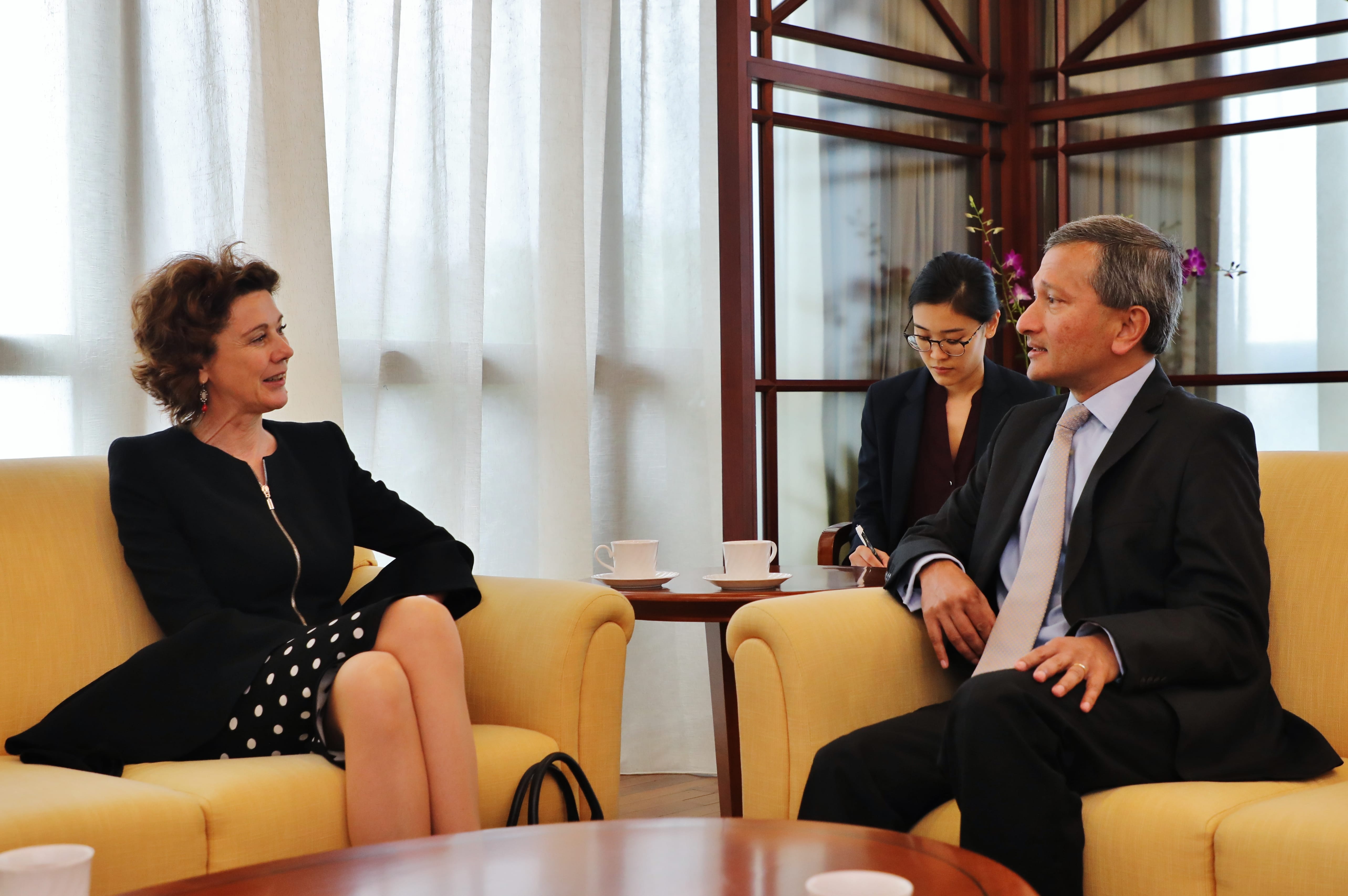 Two people in business attire seated on yellow chairs, another taking notes in the background.